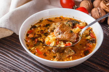 Georgian soup. Kharcho with rice, tomato, beef, garlic and herbs in bowl on wooden table