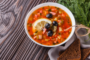 Traditional Russian meat soup Solyanka in bowl on rustic wooden table