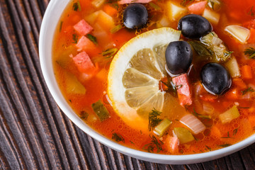 Traditional Russian meat soup Solyanka in bowl on rustic wooden table