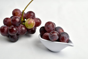 Loose grapes placed in a saucer, with diffuse background showing a bunch of grapes and envelope placed on a white tablecloth