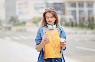Woman walking and using a smart phone on a city street - Millennial Girl sending a text message using an app on her smart phone and drinking coffee
