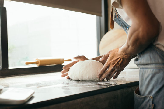 close-up of human hands in the apron knead the dough on a black wooden table, sprinkle with flour.Making dough by hands at bakery.