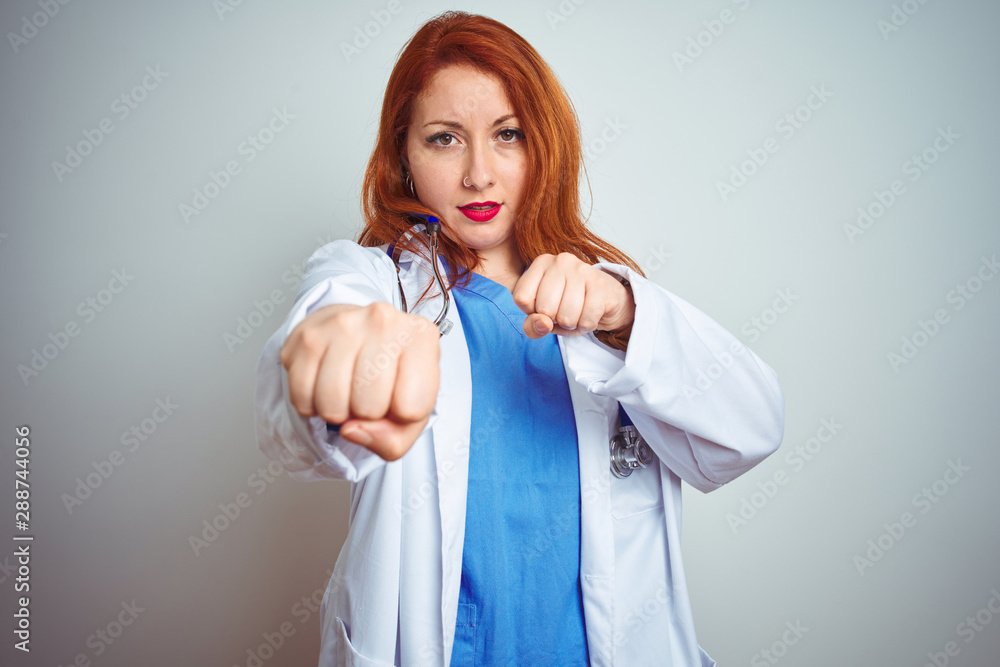 Sticker young redhead doctor woman using stethoscope over white isolated background punching fist to fight, 