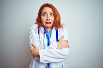 Young redhead doctor woman using stethoscope over white isolated background shaking and freezing for winter cold with sad and shock expression on face