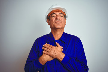 Handsome middle age worker man wearing uniform and helmet over isolated white background smiling with hands on chest with closed eyes and grateful gesture on face. Health concept.