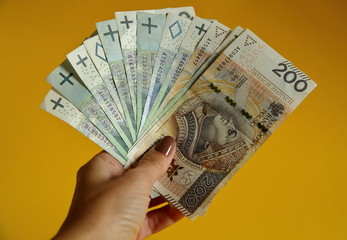 Pilik banknotów 200, 100 i 50 złotych polskich w dłni młodej kobiety, z bliska, na żółtym tle