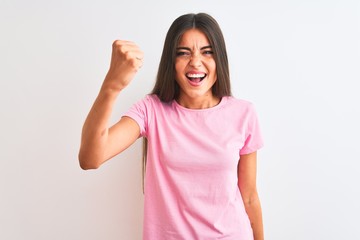 Young beautiful woman wearing pink casual t-shirt standing over isolated white background angry and mad raising fist frustrated and furious while shouting with anger. Rage and aggressive concept.