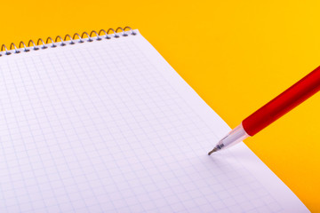 A red pen writes a text, letter or reminder on a white sheet of paper from a notebook on a spring that lies on an orange background