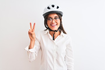 Beautiful businesswoman wearing glasses and bike helmet over isolated white background showing and pointing up with fingers number two while smiling confident and happy.