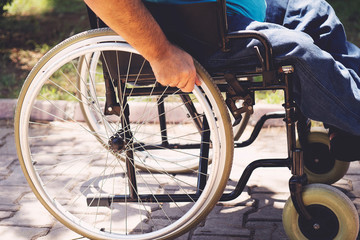 Close up photo of Young disabled man holding wheelchair outside in park