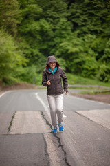 One mature woman, running outdoors on a asphalt road, in a nature.