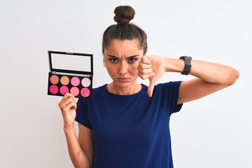 Young beautiful woman holding makeup standing over isolated white background with angry face,...