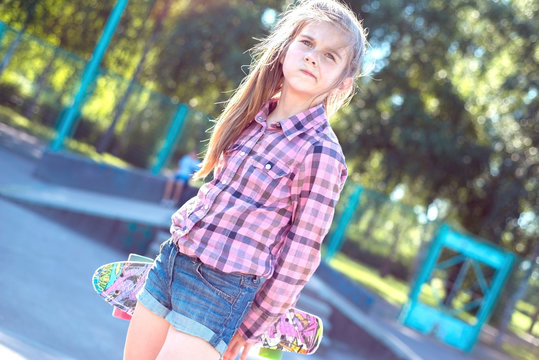 portrait of a little teenage girl, walking down the street, holding a colorful skateboard, active lifestyle of children