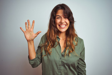 Young beautiful woman wearing green shirt standing over grey isolated background showing and pointing up with fingers number five while smiling confident and happy.