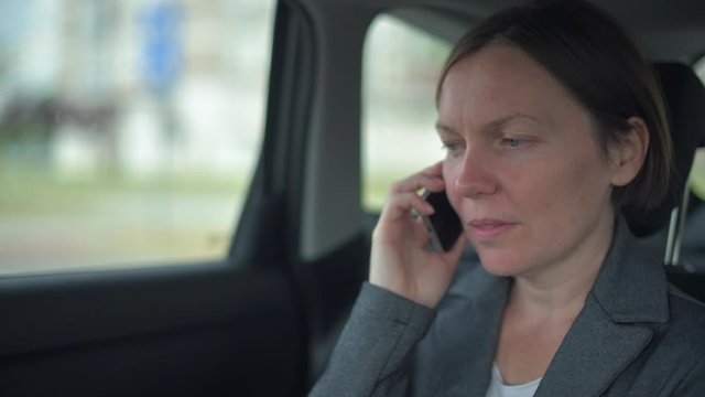 Businesswoman talking on mobile phone on car back seat
