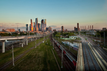 Moscow City, a district of skyscrapers, Moscow, Russia, the sunset is reflected in the buildings, in the foreground - the railway, train, road factory pipes and residential buildings in the distance