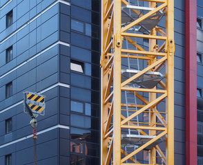 close up of the tower of a yellow construction crane with steel ladders lifting a hook with chain against a modern black building under construction