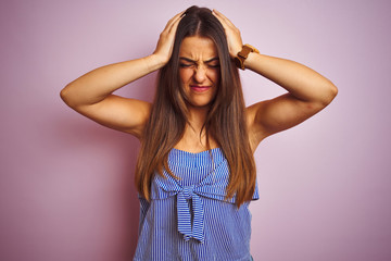 Fototapeta premium Young beautiful woman wearing striped dress standing over isolated pink background suffering from headache desperate and stressed because pain and migraine. Hands on head.