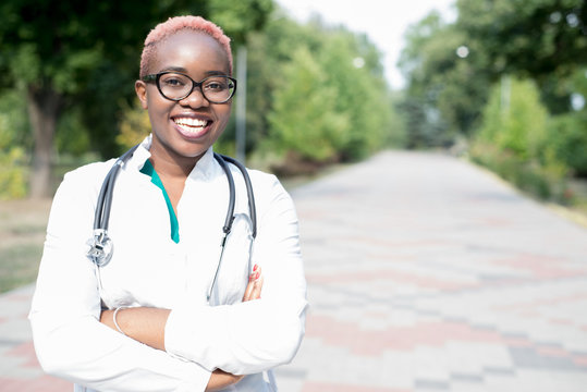Portrait of a young black girl, a doctor in a white coat, with a phonendoscope. Smiling looking at camera, outdoor