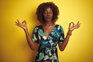 Young african afro woman wearing summer floral dress over isolated yellow background relax and smiling with eyes closed doing meditation gesture with fingers. Yoga concept.