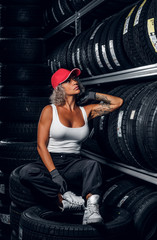 Sexy woman in red cap is chilling at tyre storage while posing for photographer.