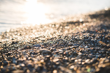 Small stones by the sea with bokeh effect. Blurred decorative background, place for text. Summer wallpaper, sunny sunset light.