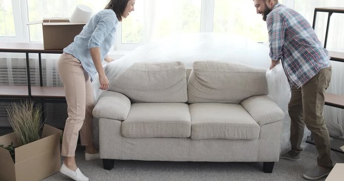 Happy young couple unpacking and jumping on sofa in new apartment