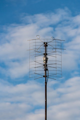 One metallic television antenna on the blue sky with white clouds background