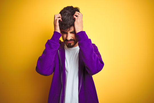 Young man with tattoo wearing sport purple sweatshirt over isolated yellow background suffering from headache desperate and stressed because pain and migraine. Hands on head.