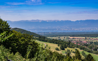 Fototapeta na wymiar City landscape in the mountains, hills, fields, forests, green meadows, lakes in the distance and blue sky with clouds,focus area in the city.Town Bons-en-Chablais, Haute-Savoie in France.