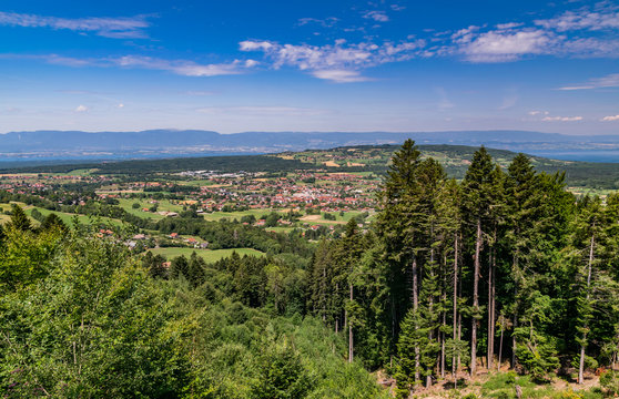  City landscape in the mountains, hills, fields, forests, green meadows, lakes in the distance and blue sky with clouds,focus area in the city.Town Bons-en-Chablais, Haute-Savoie in France.