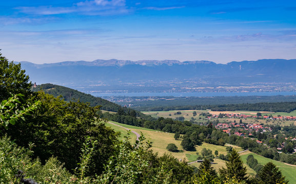  City landscape in the mountains, hills, fields, forests, green meadows, lakes in the distance and blue sky with clouds,focus area in the city.Town Bons-en-Chablais, Haute-Savoie in France.