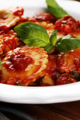 Ravioli with tomato sauce garnished with parmesan cheese and basil on rustic table