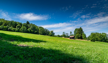 View of a small wooden house on a mountain slope with a green meadow and the blue sky with white clouds,focus plane on the cottage.Department of Haute-Savoie in France.
