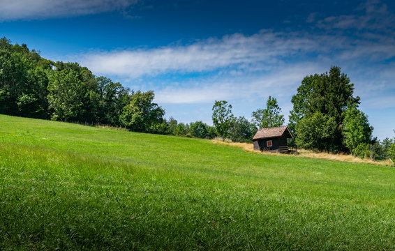 View of a small wooden house on a mountain slope with a green meadow and the blue sky with white clouds,focus plane on the cottage.Department of Haute-Savoie in France.