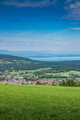 Fototapeta na wymiar City landscape in the mountains, hills, fields, forests, green meadows, lakes in the distance and blue sky with clouds,focus area in the city.Town Bons-en-Chablais, Haute-Savoie in France.