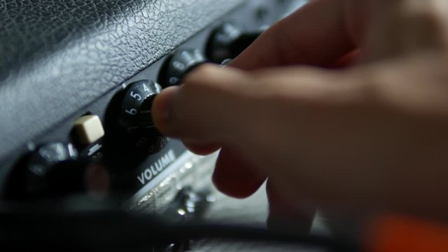 Guitarist adjusting volume and tone knob on guitar amplifier