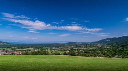 Fototapeta premium City landscape in the mountains, hills, fields, forests, green meadows, lakes in the distance and blue sky with clouds,focus area in the city.Haute-Savoie in France.