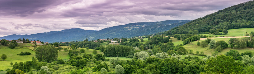Fototapeta na wymiar Panorama view of the mountain landscape, trees, forests on the slopes of hills and farmhouses with a cloudy sky in the background,focus plane in the center.Haute-Savoie in France.