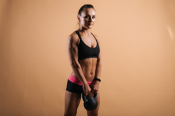 Sporty young woman with perfect muscular body in black sportswear is standing with 12 kg kettlebell...