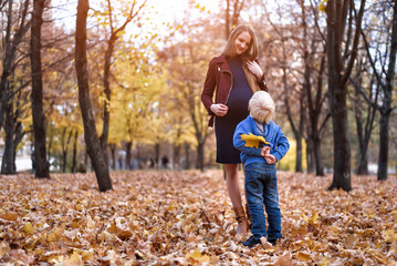 Little blond boy hid behind a yellow leaf. Wants to give mom. Autumn park on the background
