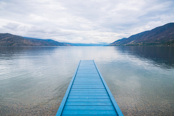 Blue painted dock on lake with view of mountains and cloudy sky