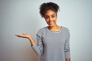 African american woman wearing navy striped t-shirt standing over isolated white background smiling cheerful presenting and pointing with palm of hand looking at the camera.