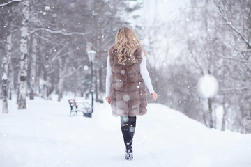girl in a fur vest walks in the winter outside / adult young model in winter clothes fur