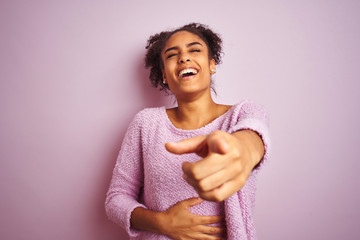 Young african american woman wearing winter sweater standing over isolated pink background laughing at you, pointing finger to the camera with hand over body, shame expression