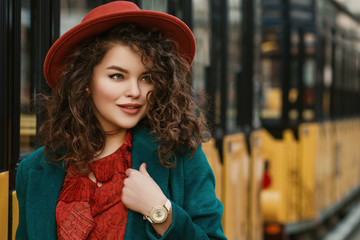 Outdoor close up portrait of young happy smiling fashionable curly lady wearing stylish orange hat,...