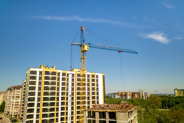 Apartment or office tall building under construction. Working builders and tower cranes on bright...