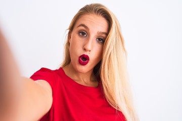 Young beautiful woman wearing t-shirt make selfie by camera over isolated white background scared in shock with a surprise face, afraid and excited with fear expression