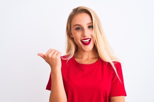 Young beautiful woman wearing red casual t-shirt standing over isolated white background smiling with happy face looking and pointing to the side with thumb up.