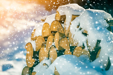 Neatly piled stack of chopped dry trunks wood covered with snow outdoors on bright cold winter sunny day, big snowflakes abstract background, Fire wood logs prepared for winter, ready for burning.
